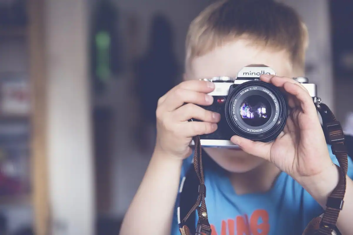 Băiat care țintește cu aparatul foto la ochi, concentrat pe punctul de focalizare ales
