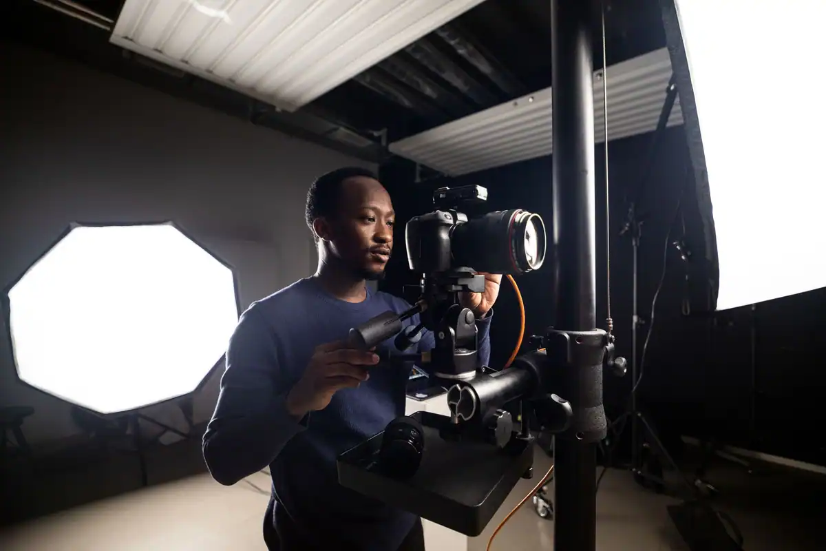 Fotograf cu aparatul pe trepied într-un studio, lângă un softbox octogonal care înmoaie lumina blitzului