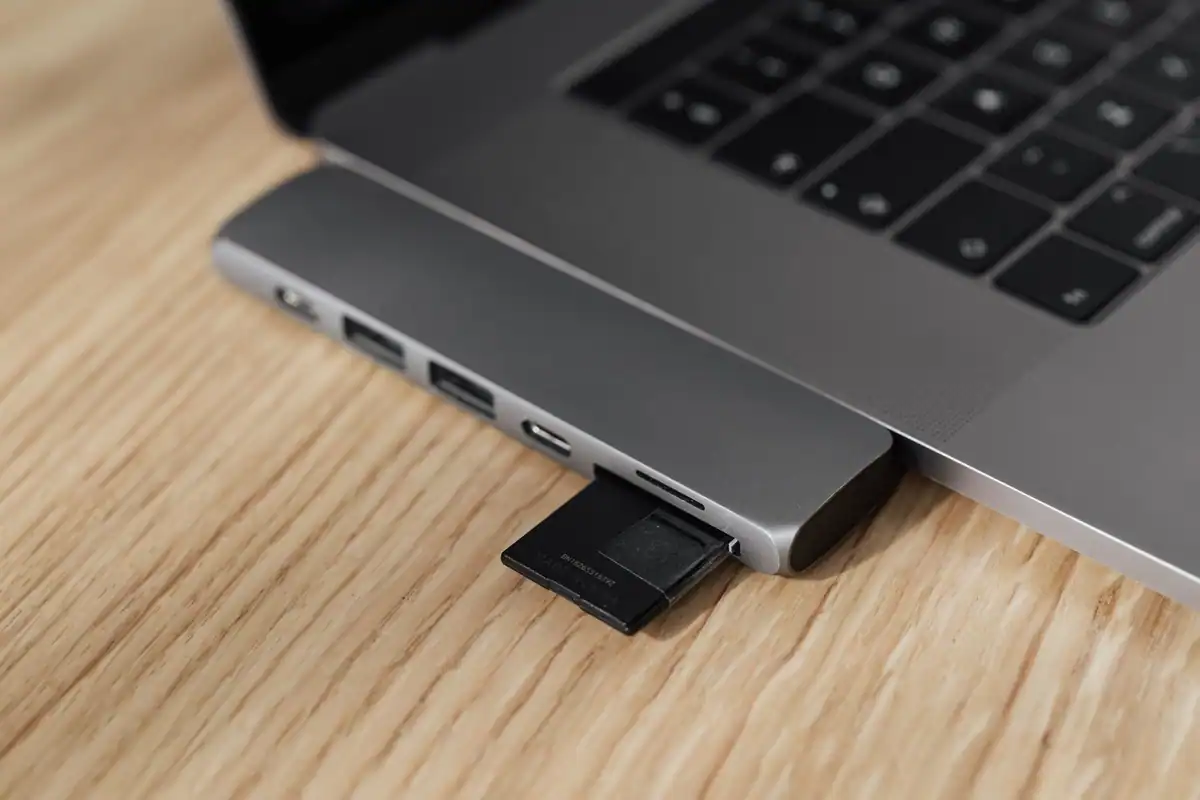 Card de memorie introdus într-un adaptor conectat la un laptop subțire, pe o masă din lemn