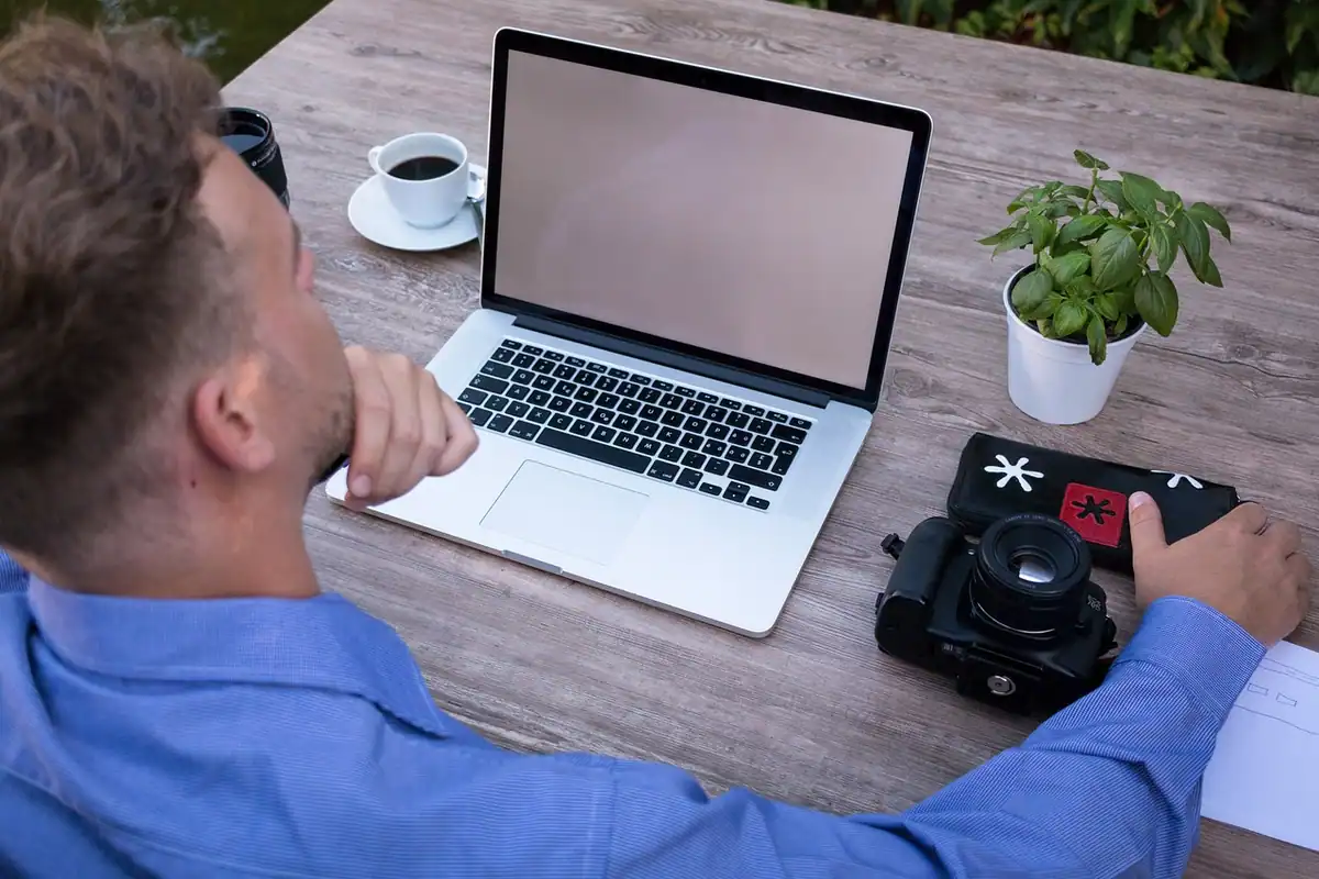 Bărbat gânditor la un laptop, cu aparatul foto pe masă, în timpul reglajelor de expunere