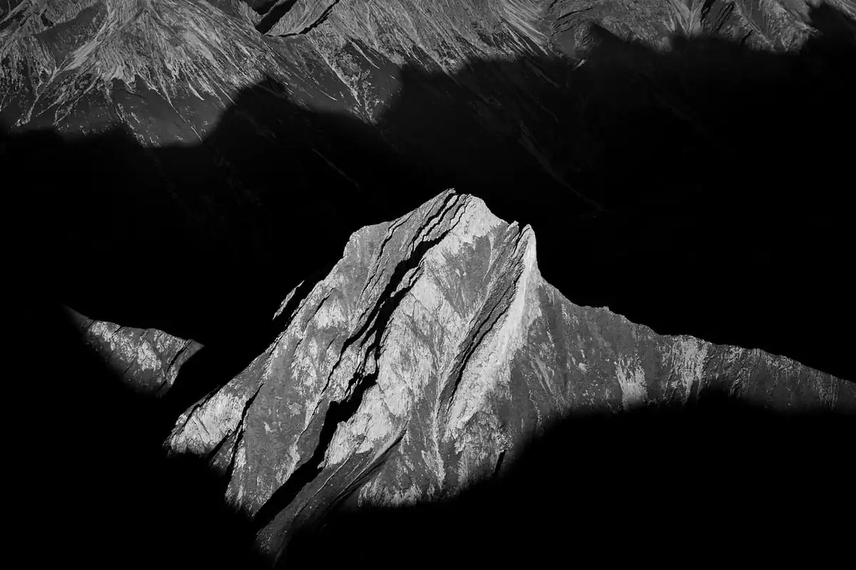 Vârf de munte alb-negru cu umbre adânci și lumini puternice, contrast accentuat