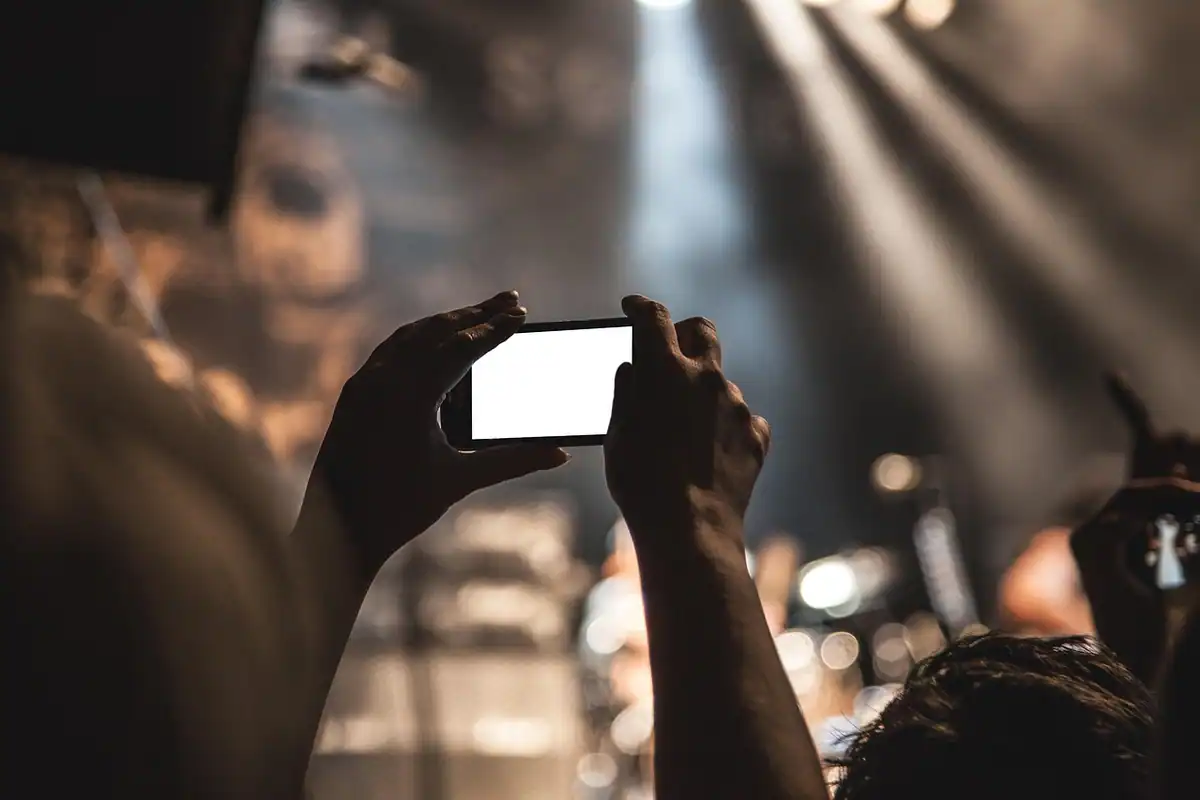 Mâini care țin telefonul ridicat deasupra mulțimii pentru a filma un concert