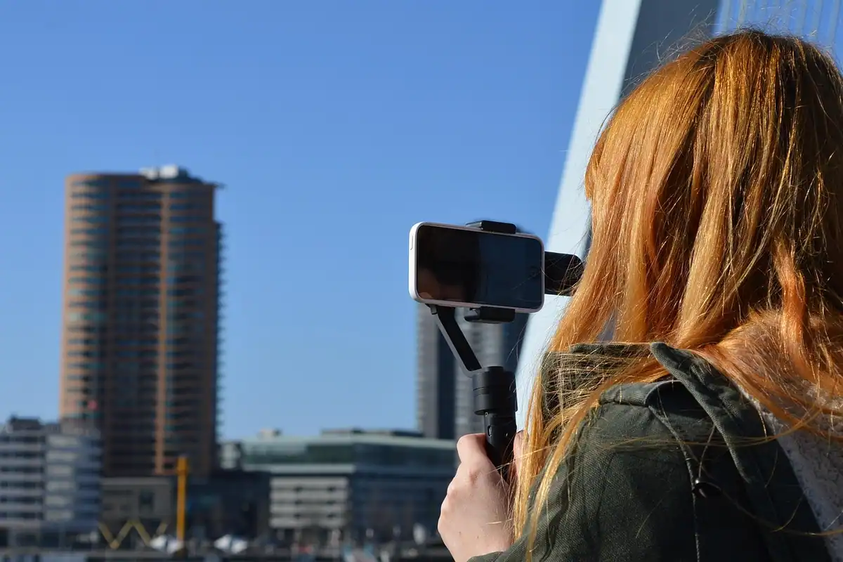 Femeie care filmează cu telefonul montat pe un stabilizator, lângă clădiri înalte