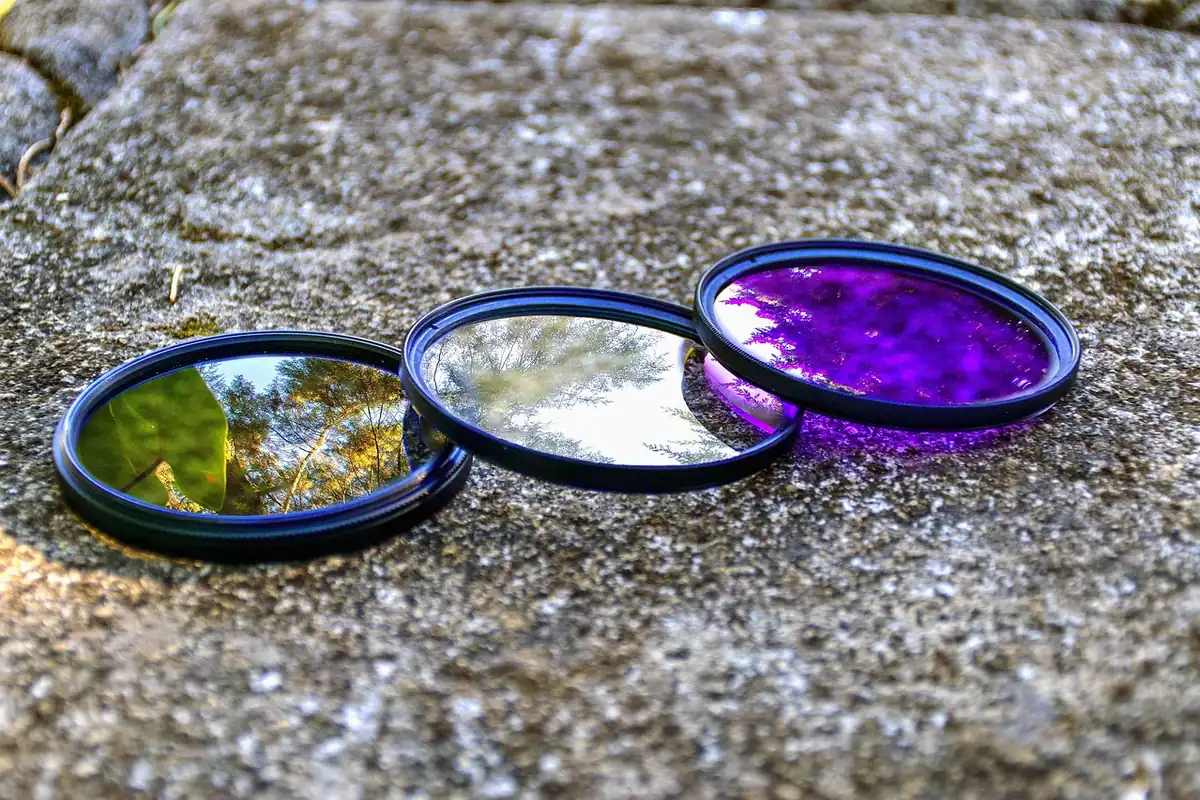Trei filtre foto rotunde așezate pe o piatră, unul cu reflexii violet