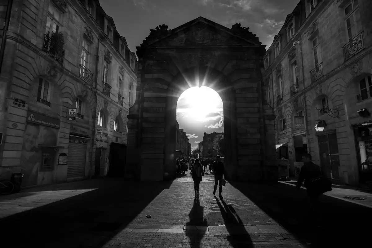 Stradă veche cu o arcadă luminată în fundal, umbre lungi și contrast puternic în alb-negru