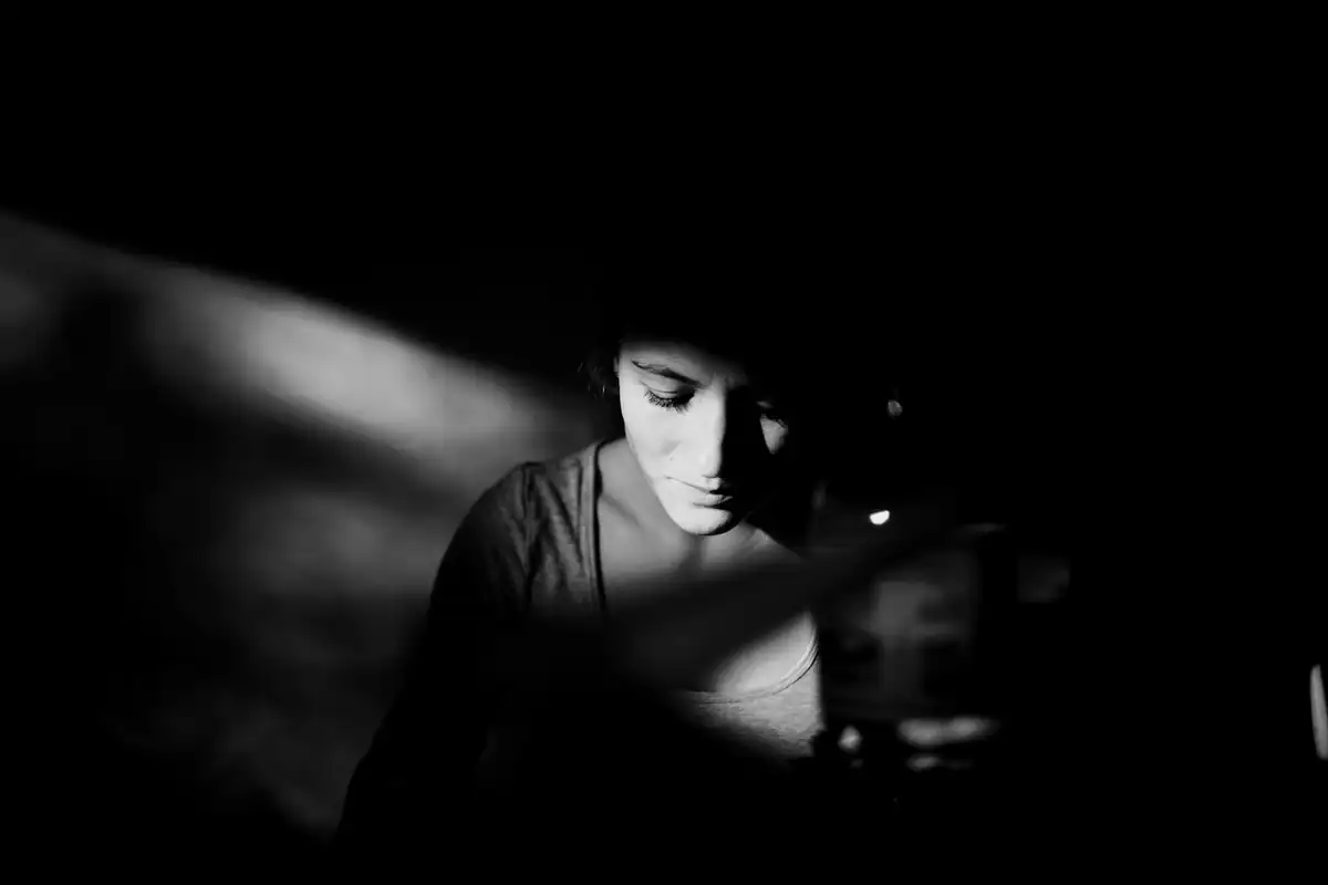 Portret alb-negru dramatic al unei persoane cu fața luminată dintr-o parte, pe fundal negru