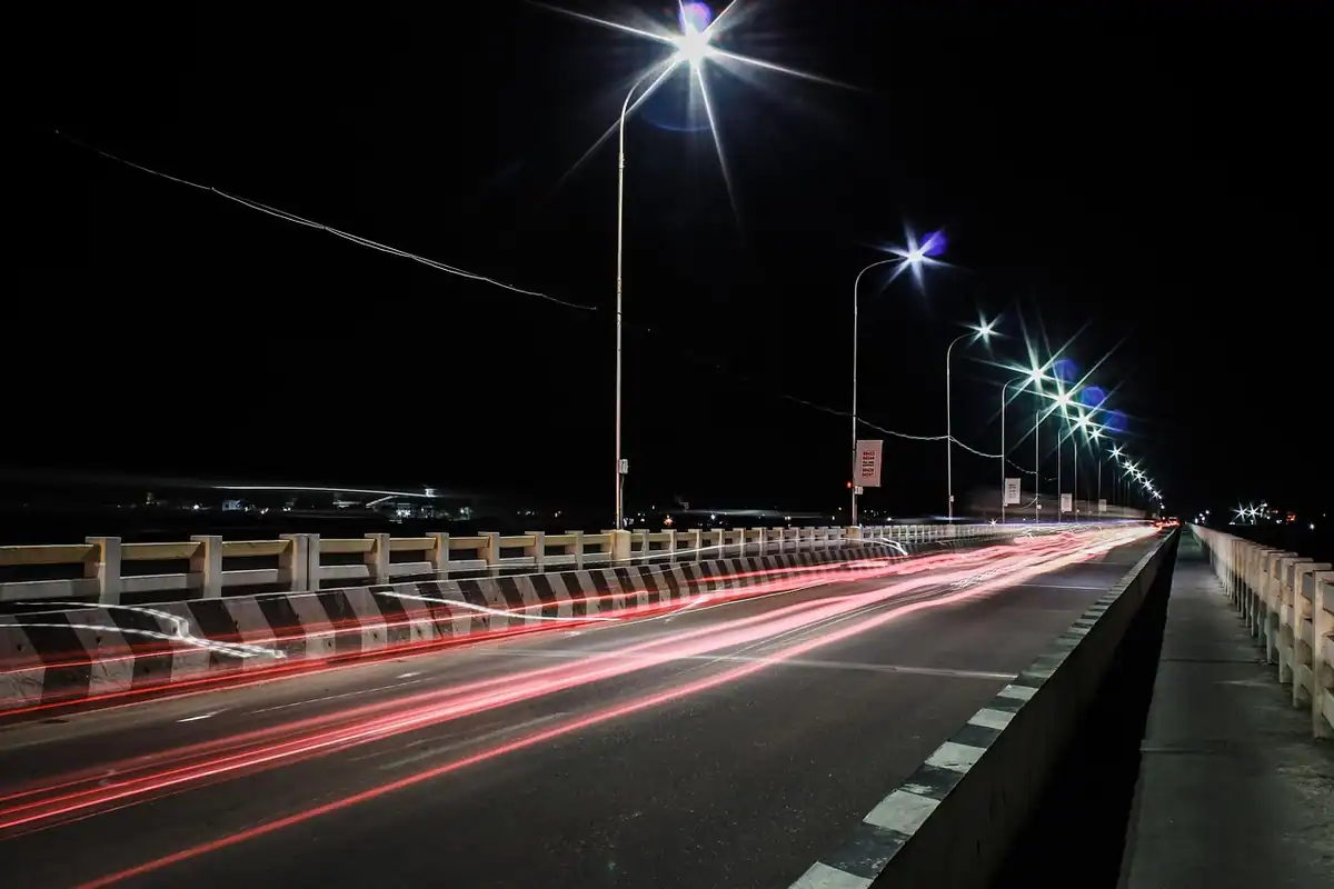 Șosea de noapte cu urme roșii de lumină de la mașini și stâlpi aprinși