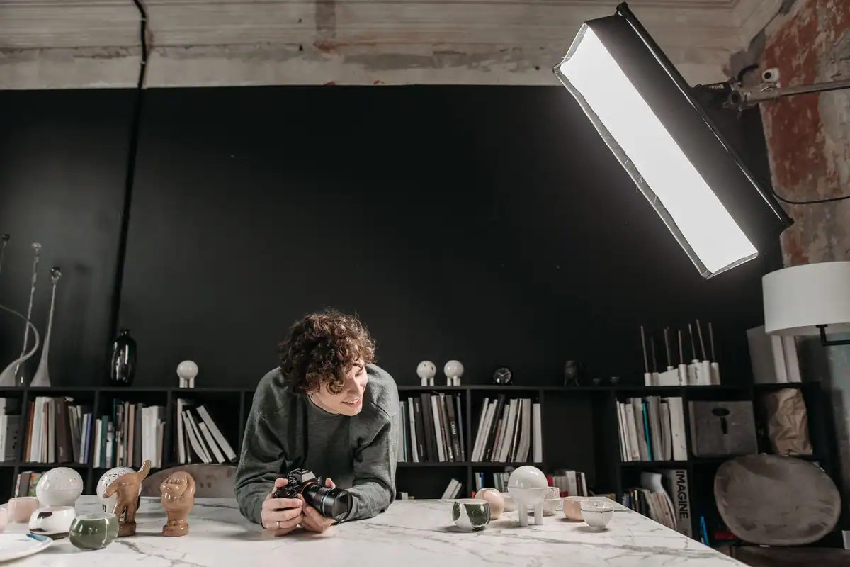Fotograf într-un studio creativ, înconjurat de obiecte din ceramică, cărți și lămpi de lumină