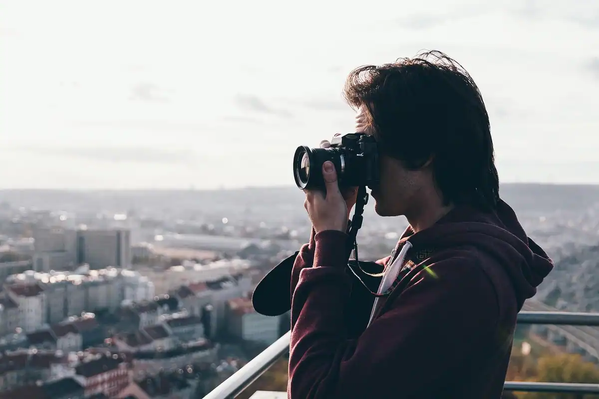 Bărbat care fotografiază panorama unui oraș de pe o terasă, cu aparatul la ochi