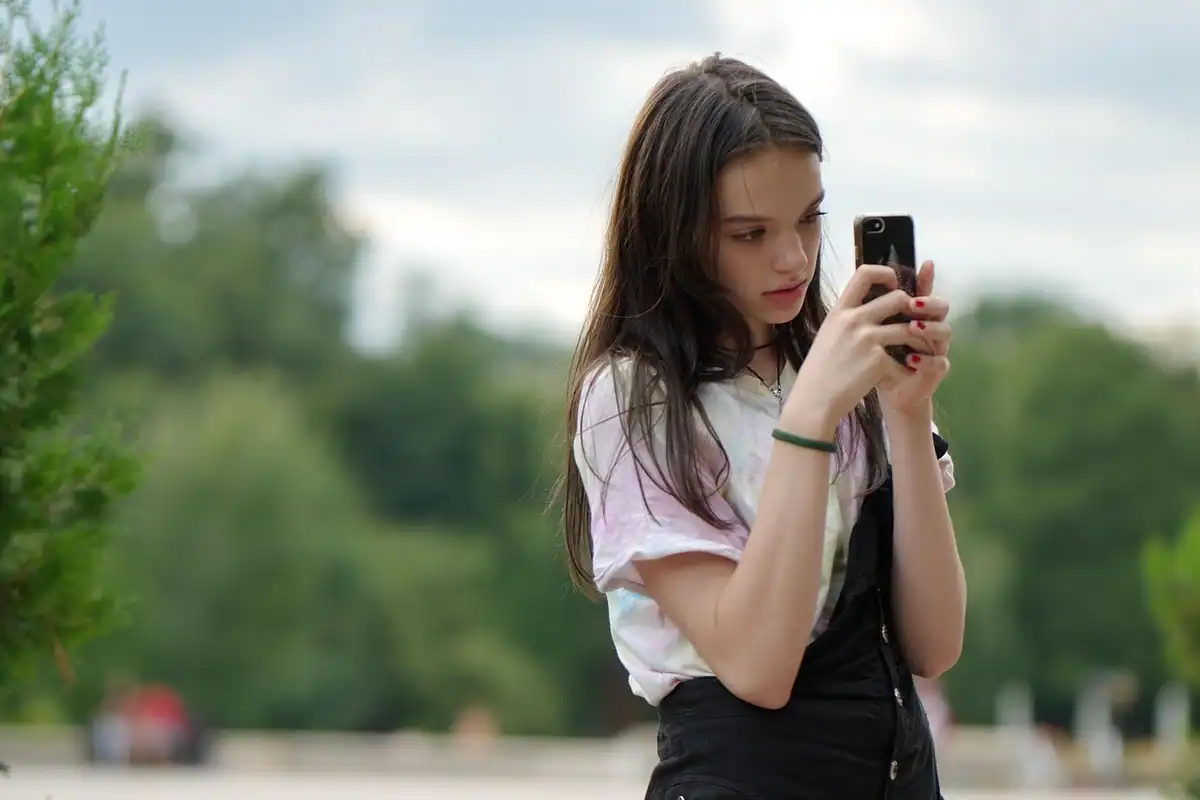 Adolescentă care fotografiază cu telefonul într-un parc, în lumină naturală moale