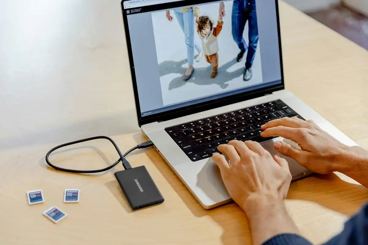 Laptop cu o fotografie deschisă în editare, un SSD și fotografii mici pe birou