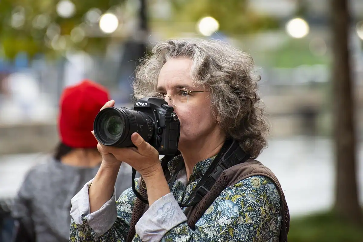 Femeie cu păr cărunt care fotografiază cu un aparat DSLR, într-un parc