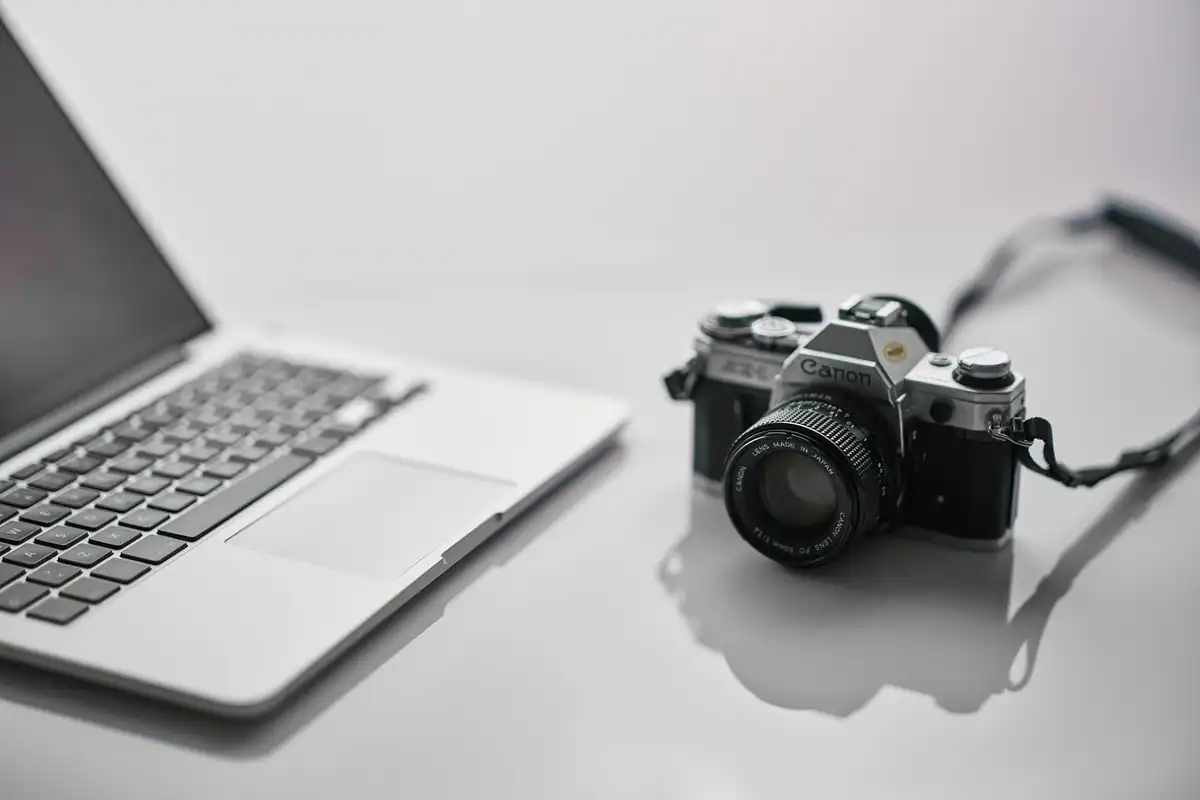 Laptop și aparat foto pe un birou alb, pentru transferul și developarea fișierelor