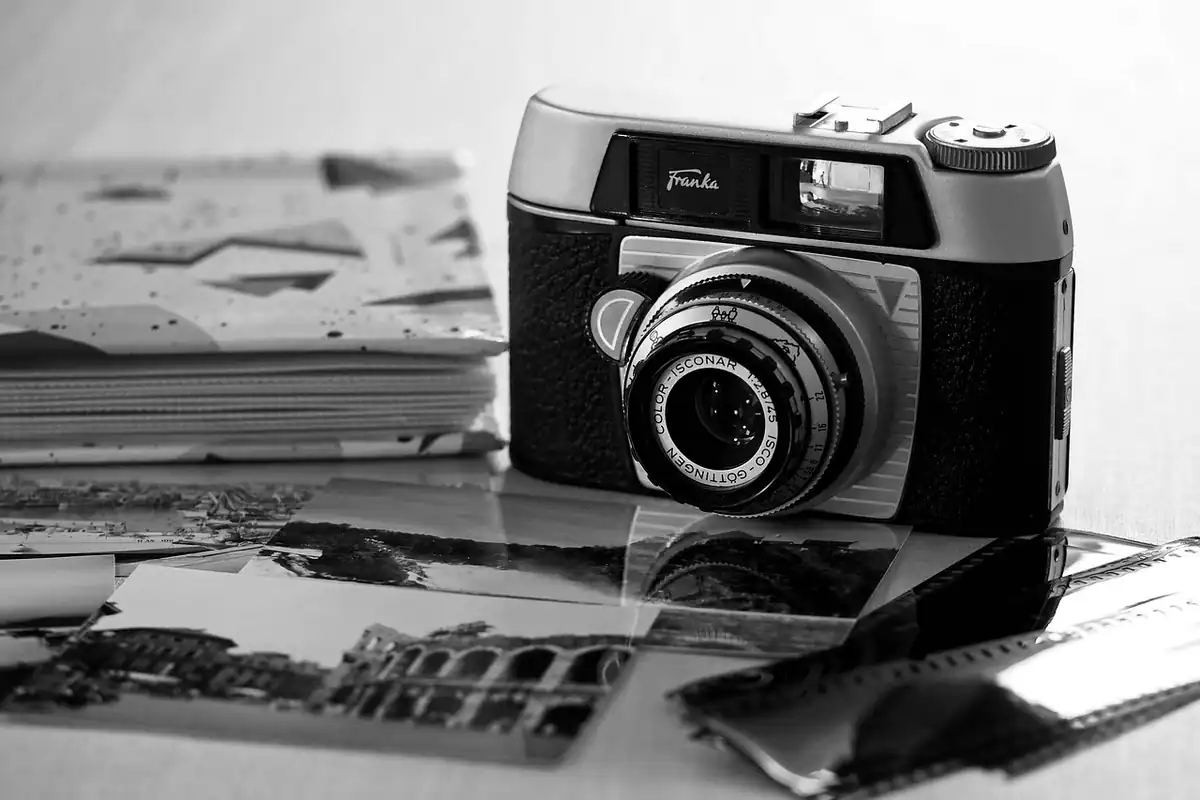 Aparat foto vechi lângă un teanc de fotografii și negative, în alb-negru
