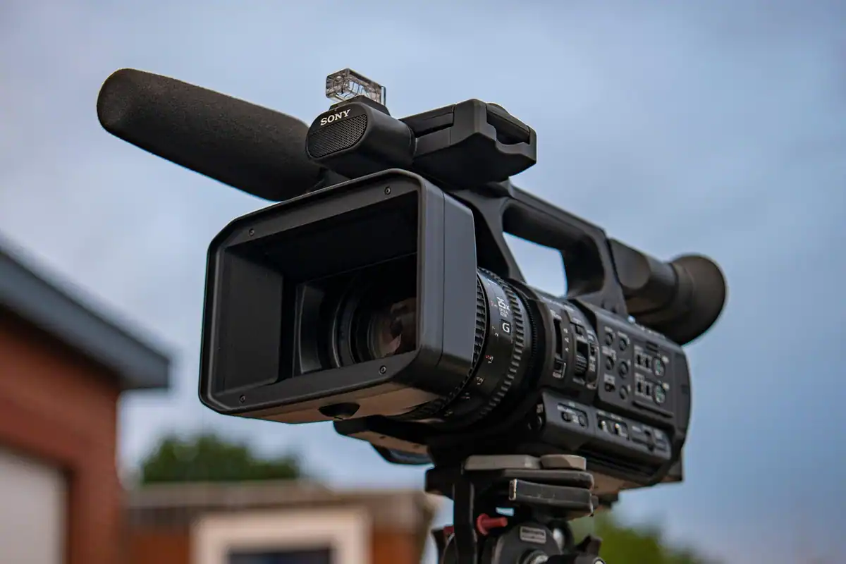 Cameră video profesională cu microfon pe trepied, sub un cer albastru senin