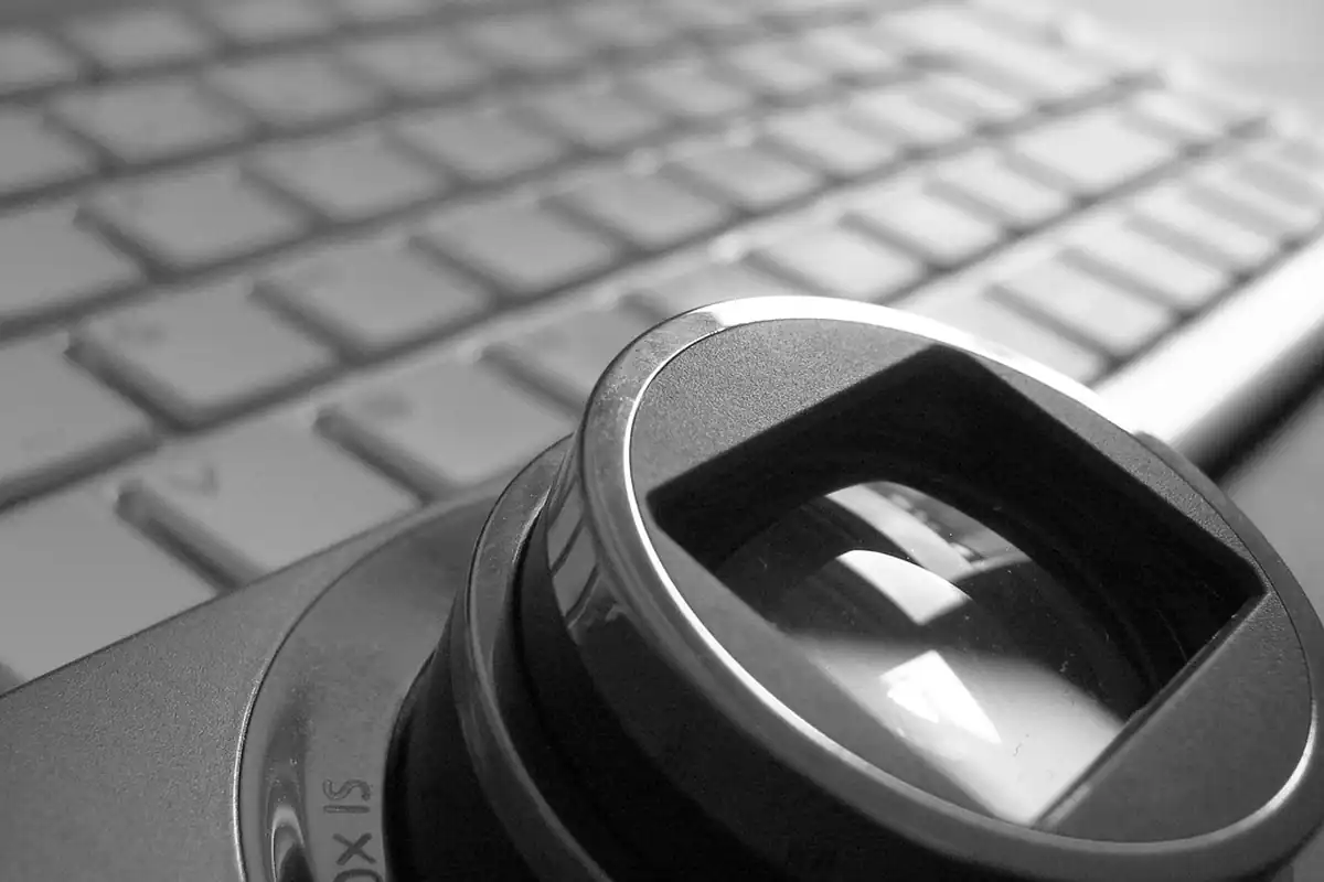 Obiectiv de aparat foto așezat pe o tastatură, aproape, cu sticla în prim-plan