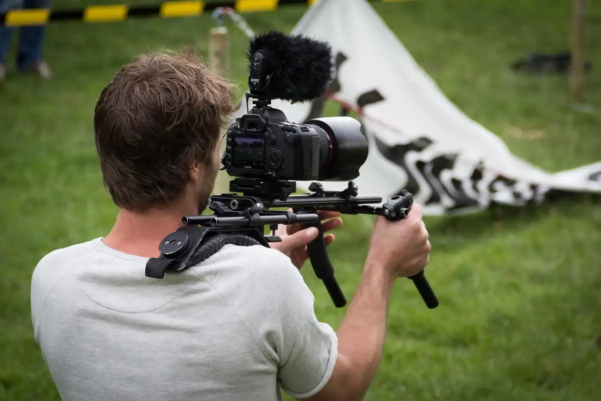 Operator cu cameră montată pe un suport de umăr, filmând în iarbă cu mișcări line